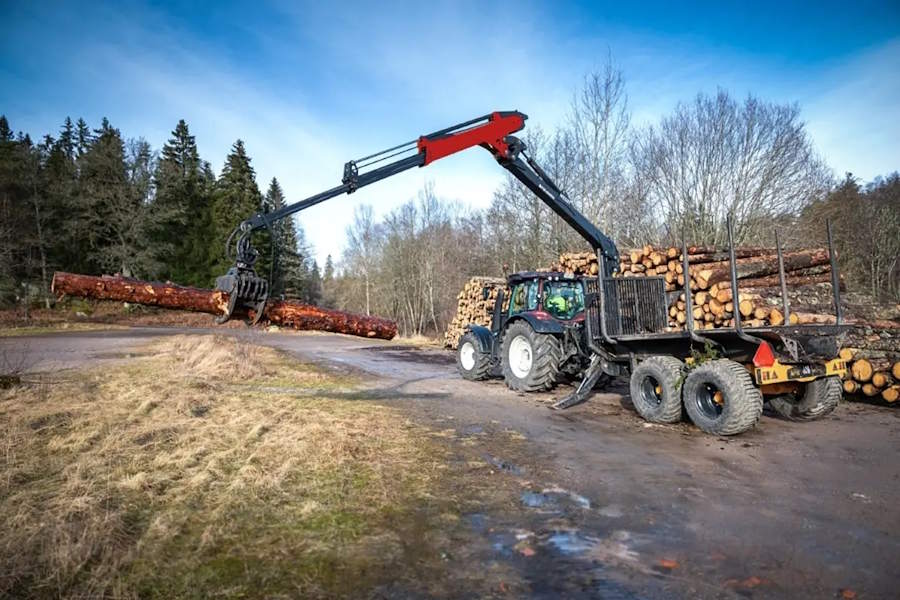 Timber trailer with an attached hydraulic crane, pulled by a tractor. This setup is from FTG which is a major player in forestry machines.